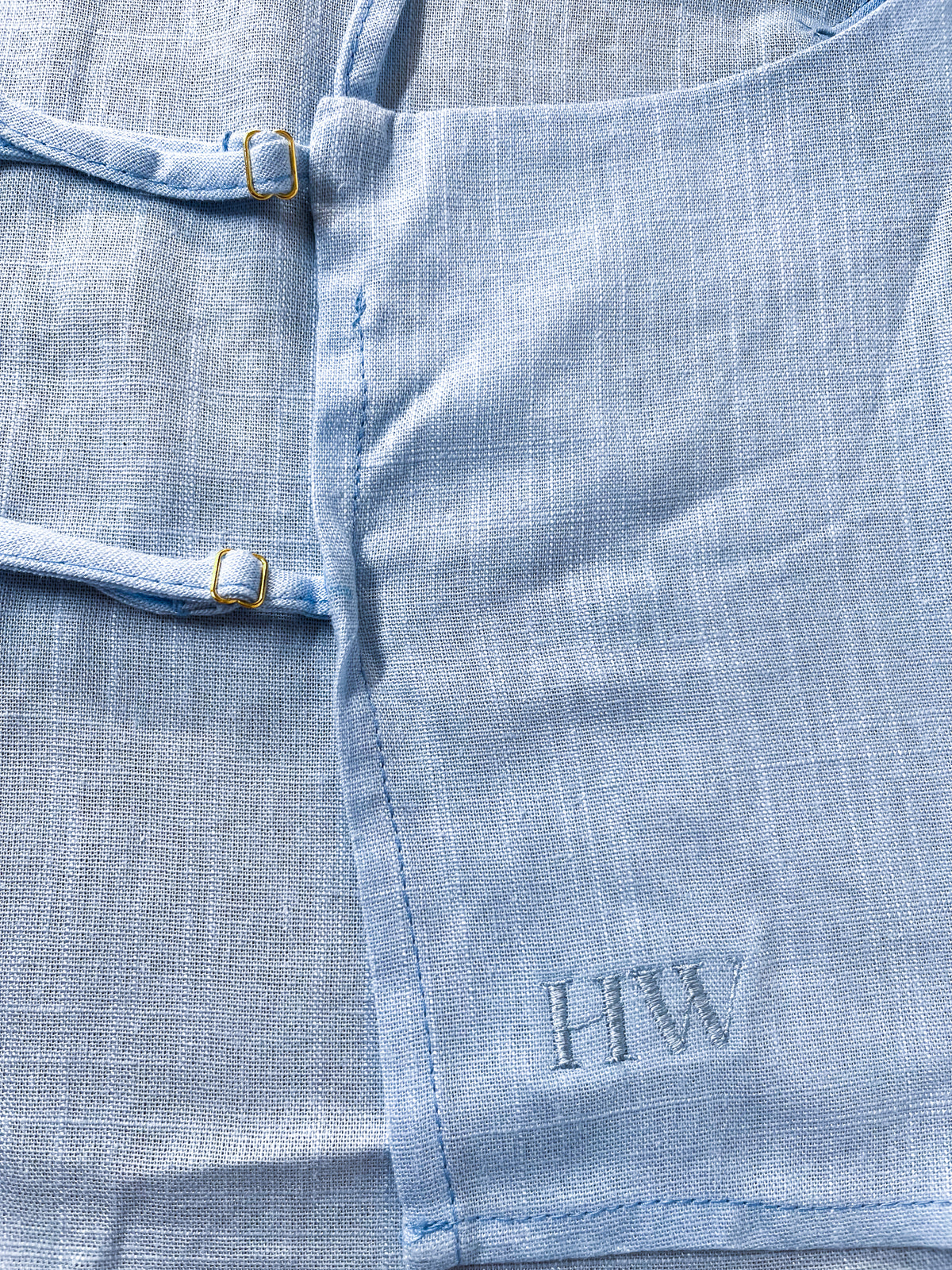 Close-up of light blue linen texture with tonal HW embroidery and strap buckles