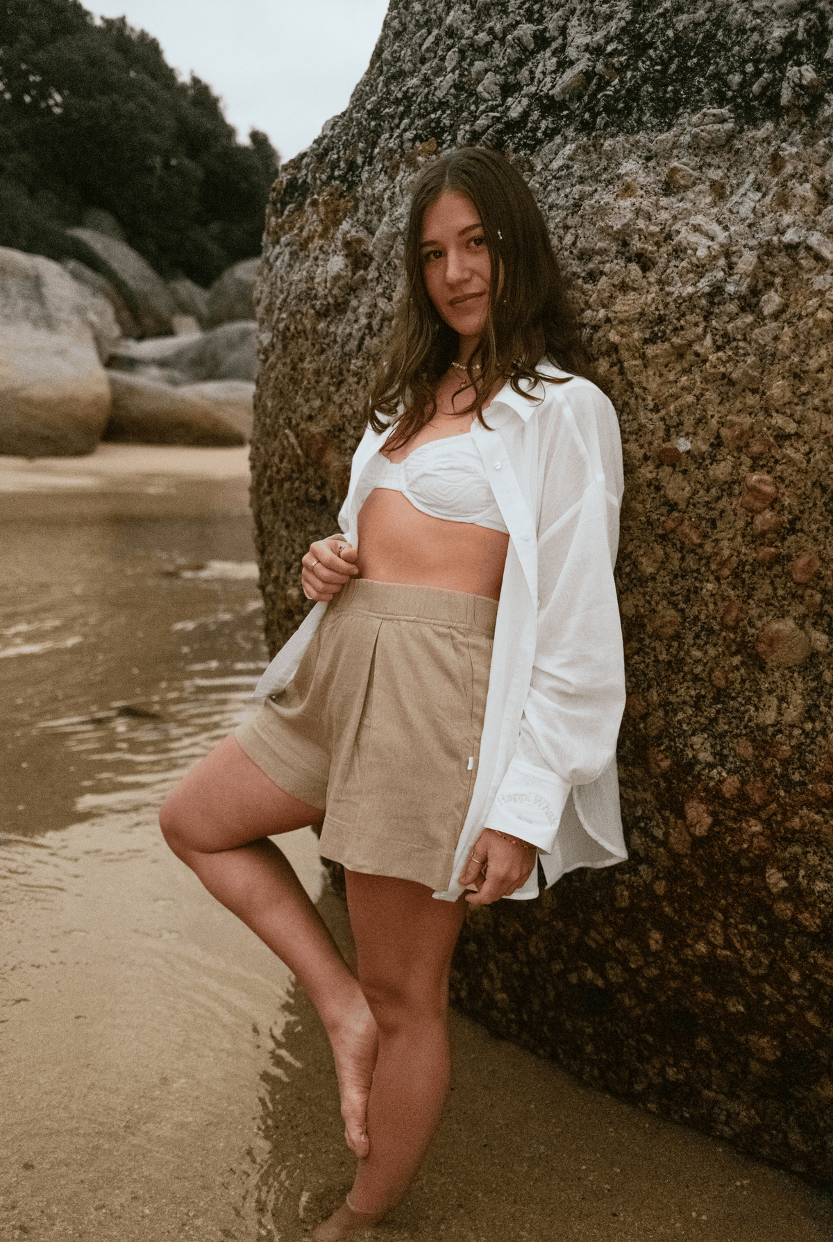 Woman leaning on a boulder in Beach Babe Shorts with an open white shirt