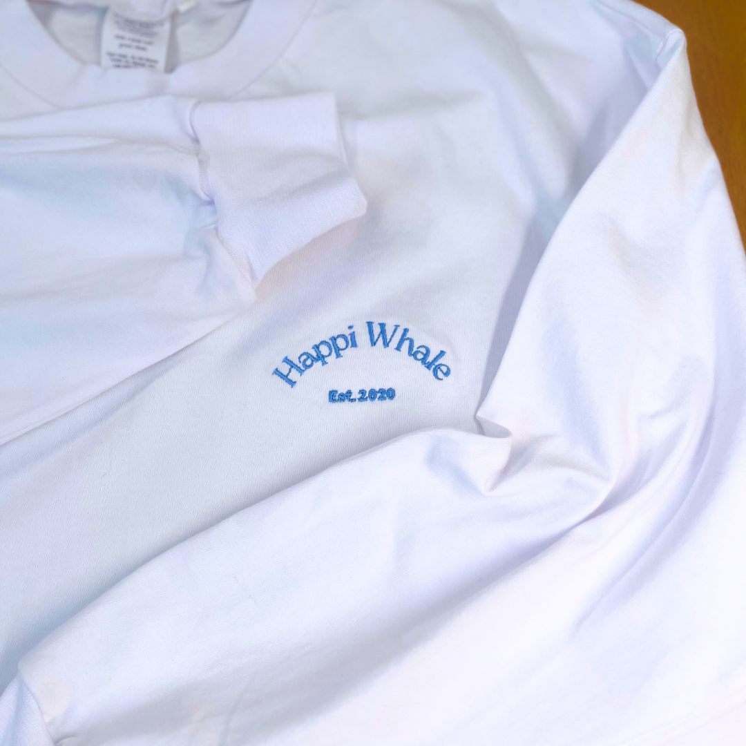 Detail of the Happi Whale Est. embroidery on the white cotton crew