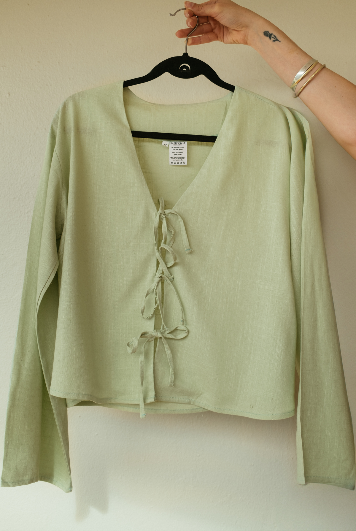 Sage green Cove Top on a hanger, showing the deep V-neck and three front ties
