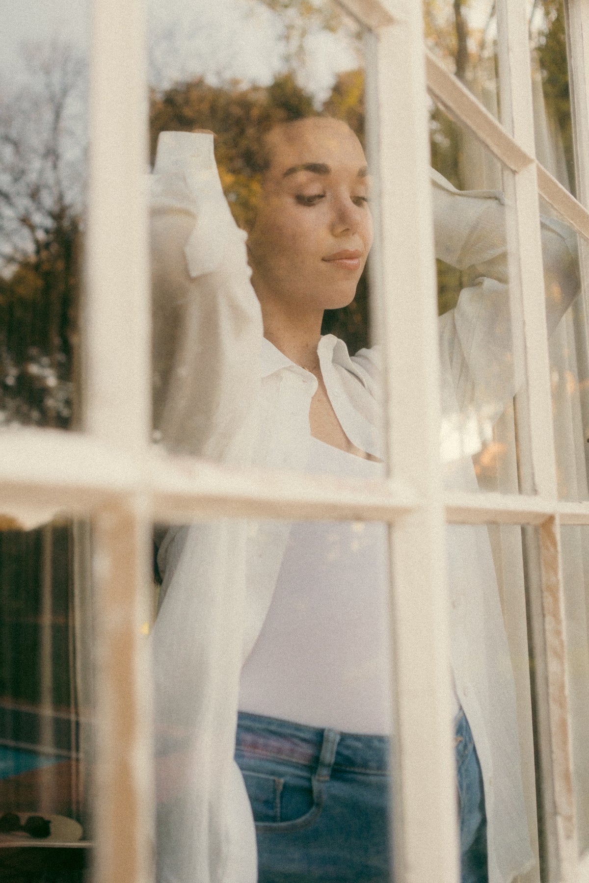 Woman behind a window wearing the white Hillie's Breeze Shirt with jeans