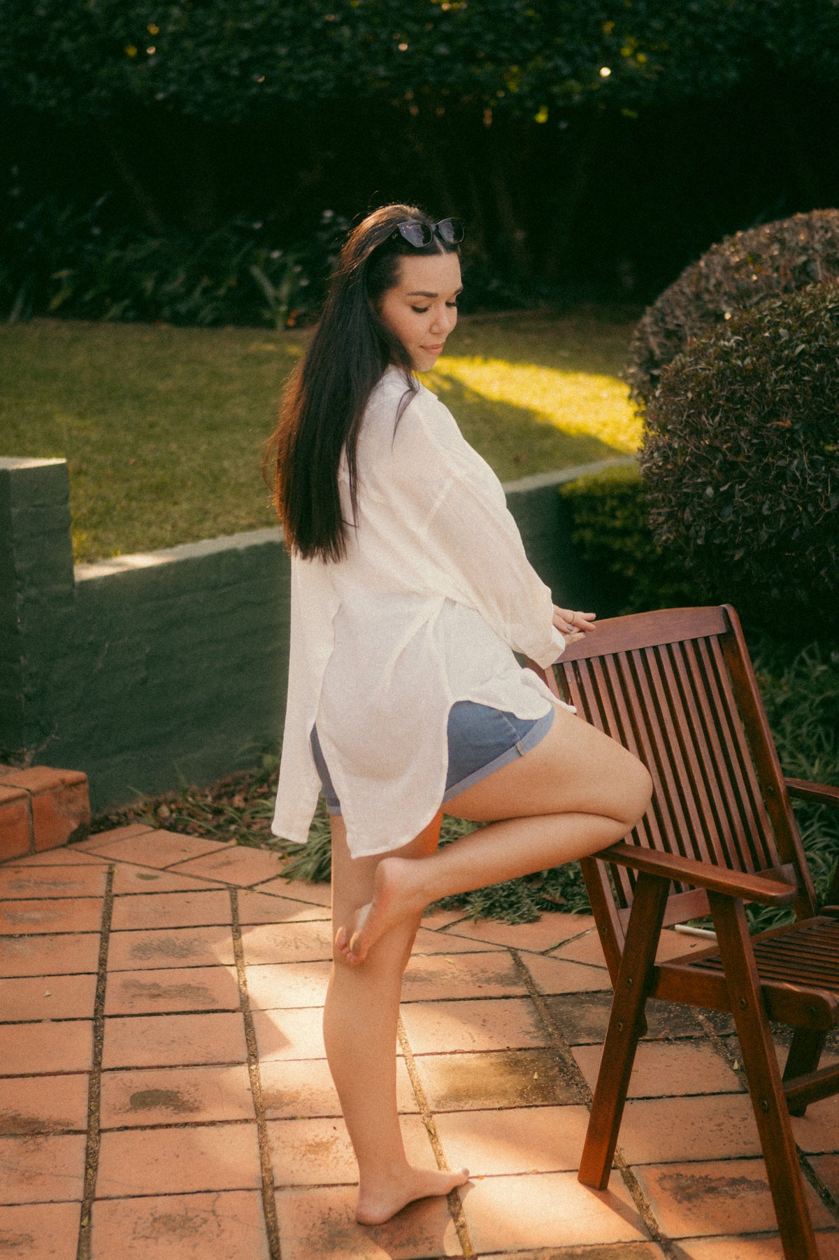 Side view of the relaxed white Hillie's Breeze Shirt with denim shorts on a sunny patio