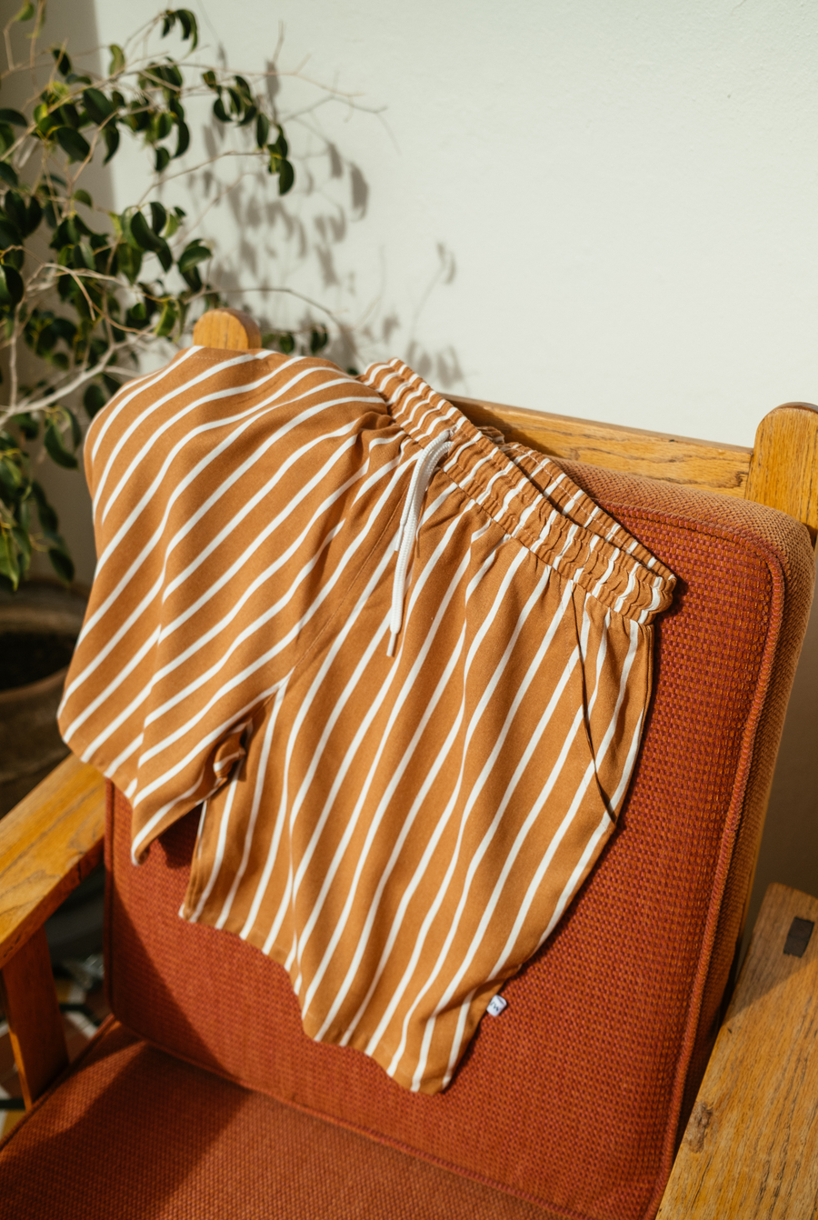 The Men's Coastal Shorts in rust and white vertical stripes on a terracotta armchair