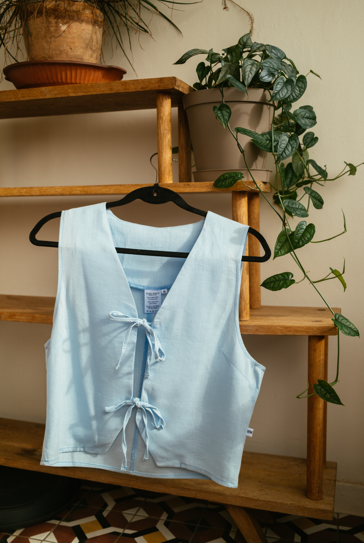 Sky Tie Vest in light blue linen on a hanger, showing the front tie closures